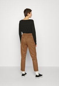 T-shirt de mangas longas preta combinada com calças castanhas risca de giz e sapatilhas pretas. O conjunto apresenta uma cintura elástica e detalhes de costura sutis.