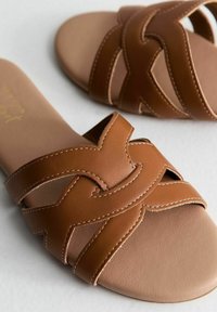 Bruna lädersandaler med halkskydd och ett korskorsdesign med kontrasterande sömmar, platt sula och en slät, texturerad fotbädd.