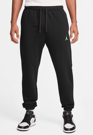 Mand iført sorte Jordan joggingbukser med elastiske manchetter og snøre, kombineret med sorte og hvide Jordan sneakers.