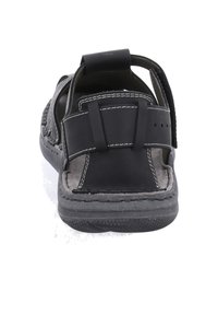 Musta sandaali, jossa on teksturoitu kumipohja, nahkainen yläosa, säädettävä hihna ja kontrastiväriset valkoiset tikkaus. Avoin malli hengittävyyden parantamiseksi.