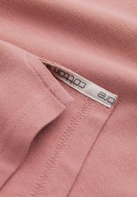 Gros plan d'un tissu en coton rose avec un détail de couture et une étiquette blanche portant la mention "one cotton" cousue dans la couture.