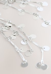 Silver chain featuring multiple round and oval discs, varying in finish, with a smooth, reflective surface and linked design.