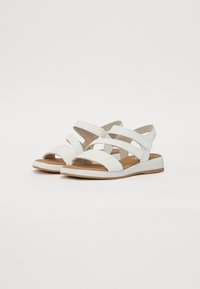 Sandales blanches avec plusieurs brides croisées, un bout rounded et un petit talon rembourré. Fabriquées en cuir doux avec une semelle en caoutchouc.