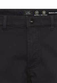 Dunkelblaue Hosen mit Knopfverschluss, hochwertigem Stretchmaterial und einer Sicherheitstasche, mit einem Etikett, das Marke und Eigenschaften anzeigt.