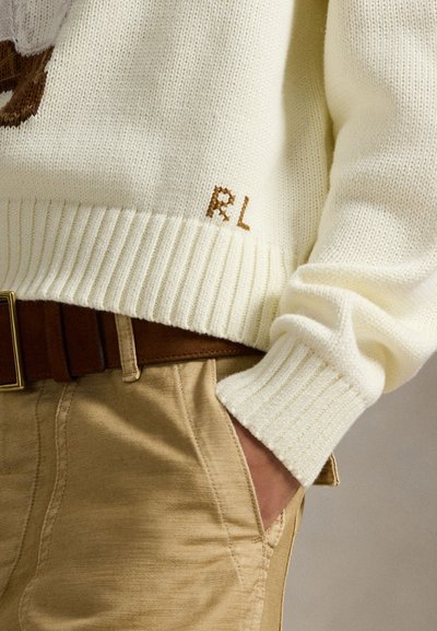 Κρεμ πουλόβερ πλεκτό με ριμπ μανσέτες και τελείωμα, με καφέ λογότυπο RL. Συνδυασμένο με καφέ παντελόνι και καφέ ζώνη.