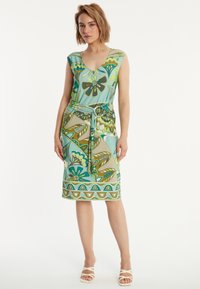 Robe multicolore avec un décolleté en V, des manches courtes et une taille cintrée avec une ceinture. Le tissu affiche des motifs floraux et de feuilles dans des tons de vert et de bleu.