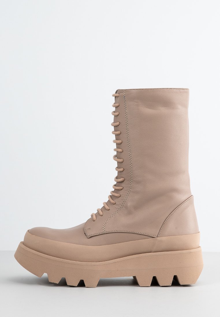 Bota de caña alta beige con cordones, con suela de goma gruesa y texturizada, hecha de cuero suave.