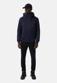 Granatowa kurtka z kapturem, zapinana na zamek, z kieszeniami bocznymi i elastycznymi mankietami, w połączeniu z czarnymi spodniami slim-fit i czarnymi butami typu high-top.