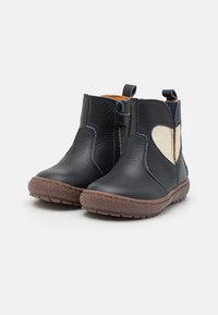 Bottines en cuir bleu avec un accent en forme de coeur beigne, bout arrondi et semelle en caoutchouc texturé marron ; dotées de tirettes pour un enfilage facile.
