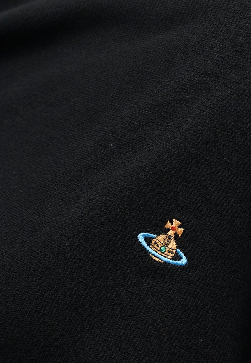 Black fabric with a small embroidered design of a gold orb topped with a cross, encircled by a blue ring and a small green gem.