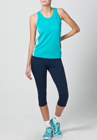 Turkos atletisk linne med vita sidosyningar, kombinerat med marinkorta leggings. Modell som bär teal löparskor.