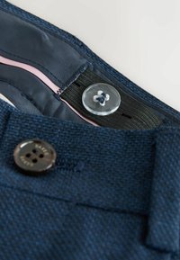 Marineblauer strukturierter Stoff einer Hose mit einem glatten Innenfutter. Verfügt über einen klaren Knopf und einen dunklen Knopf mit vier Löchern zum Schließen.