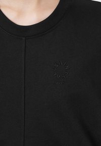 Sudadera negra con cuello redondo acanalado, textura suave y detalles de logotipo en relieve con "SAINT LONDON" en el centro.