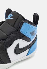 Schwarz-weißer Sneaker mit blauen Akzenten, aus synthetischen Materialien gefertigt. Verfügt über einen gepolsterten Kragen, eine strukturierte Oberseite und ein auffälliges Nike-Logo.