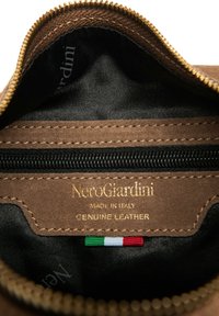 Bustina in pelle marrone autentica con etichetta logo dorata, rivestimento interno nero e chiusura a zip. Presenta un piccolo dettaglio con bandiera italiana.