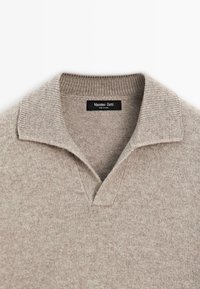 Maglione a maglia marrone chiaro con colletto a coste e scollatura a V, con un'etichetta nera visibile all'interno del collo.