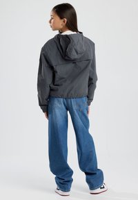 Harmaa kevyt takki, jossa on huppu, joustavat hihansuut ja selkäpaneeli, yhdistettynä väljiin sinisiin farkkuihin ja valkoisiin tennareihin.