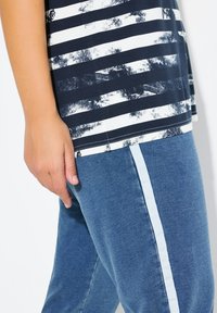 Top de rayas en azul marino y blanco con un acabado texturizado, combinado con pantalones azules que cuentan con una franja lateral de color azul claro, mostrando detalles de vestimenta casual.