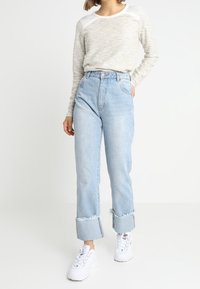 Světle šedý texturovaný top s dlouhým rukávem v kombinaci s vysokým pasem světle modré džínsy s trhaným lemem a ohrnutými manžetami, doplněné bílými teniskami.