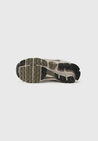 Semelle de chaussure avec un design texturé multicolore. Comprend des sections beige clair, vert et noir disposées en motif pour une adhérence.