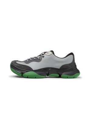 Zapatilla baja con parte superior gris, paneles negros y gris oscuro, cordones negros y suela gruesa negra y verde.