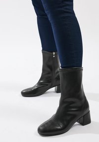 Czarne skórzane botki do kostek na słupku, z zamkiem błyskawicznym i gładką fakturą, prezentowane z dopasowanymi granatowymi spodniami.