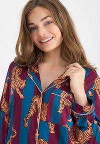 Ensemble de pyjama multicolore avec un motif rayé bleu et bordeaux orné de tigres orange. Tissu doux avec fermeture à boutons et détail de poche.