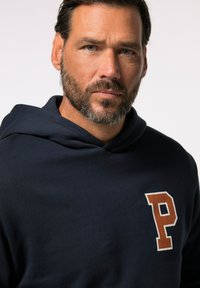 Felpa blu navy con tasca a marsupio, caratterizzata da una lettera "P" arancione a contrasto sul lato sinistro del petto. Tessuto morbido e vestibilità comoda.