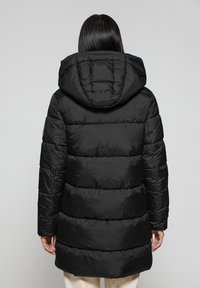 Svart puffig jacka med huva, med vertikal quiltning, medellång design och elastiska ärmslut. Slät, glänsande tygtextur.