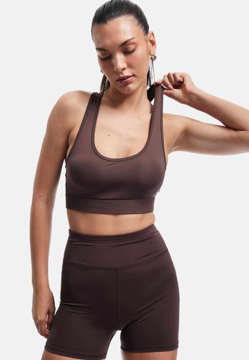 Brązowy sportowy crop top i wysokie szorty wykonane z gładkiego, elastycznego materiału z minimalną ilością szwów, z dekoltem w serek i szerokimi ramiączkami.