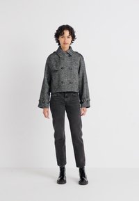Kuttet grå jakke med dobbelte knapper, stor krage og frontlommer, parret med svarte jeans og snørestøvler.
