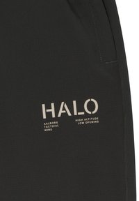 Czarna tkanina z białym napisem "HALO", "Aalborg Tactical Wing" oraz "High Altitude Low Opening" w pobliżu zszytego brzegu kieszeni.