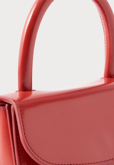 Lesklá červená kabelka s okrúhlou rúčkou a zapínaním na prešívanú klopu, zobrazená zblízka na jednoduchom pozadí.