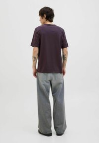 Camiseta corta de manga maroon, corte relajado, combinada con jeans de pierna ancha en gris claro. Tatuajes del tono de piel visibles en los brazos. Diseño simple, sin patrones.