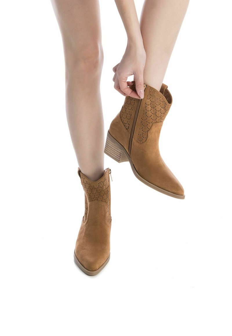 Botas de ante en color topo, con puntera afilada, diseño perforado en el puño y un tacón de madera ligera. Cremallera en el lateral.