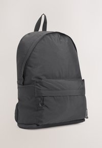 Sac à dos noir léger avec une poche zippée à l'avant et une poignée supérieure, présenté sur un fond neutre.