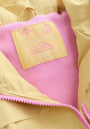 Keltainen vedenpitävä takki, jossa on pinkki fleec-vuori. Takissa on vedenpitävyyttä ja tuulenpitävyyttä kuvaavat symbolit sekä pinkki vetoketjusomiste.
