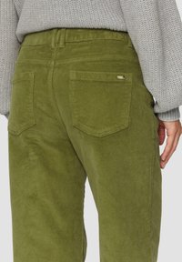 Grüne Cordhosen mit einem gerippten Textur, ausgestattet mit zwei Gesäßtaschen und einem kleinen Metalltag-Akzent in der Nähe des Bunds.
