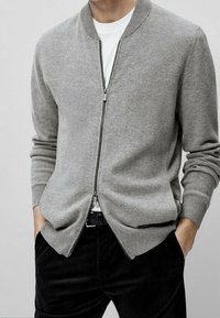 Szary kardigan na zamek wykonany z miękkiego materiału, z prążkowanym kołnierzem i mankietami, noszony na gładkiej białej koszuli, w połączeniu z ciemnymi spodniami.