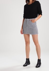 Schwarzes Langarmoberteil mit gerippter Textur, kombiniert mit einem hoch taillierten kurzen Rock mit einem schwarz-weißen Karomuster und Seitentaschen.