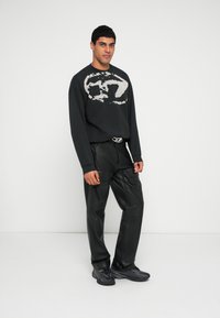 Sweatshirt preta oversized com um logótipo abstrato branco, combinada com calças cargo de couro pretas e ténis pretos às riscas.