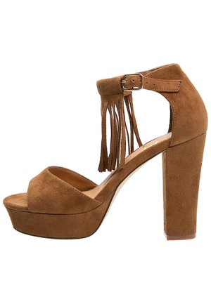 Sandalia de plataforma de ante marrón de tacón alto, con punta abierta, correa en el tobillo, cierre de hebilla y detalles de flecos en el talón.