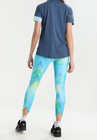 Krátký rukáv, tmavě modrý top s světle modrými akcenty, spárovaný s jasně modrými legínami, které mají vzory hor v zelené a žluté barvě a šikmé lemy.