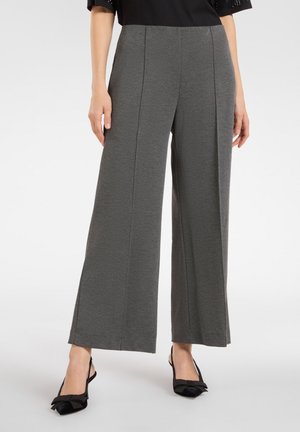 Wijde broek in donkergrijs stof, met een gladde textuur en voorplooien. Gecombineerd met zwarte schoenen met strikdetail.