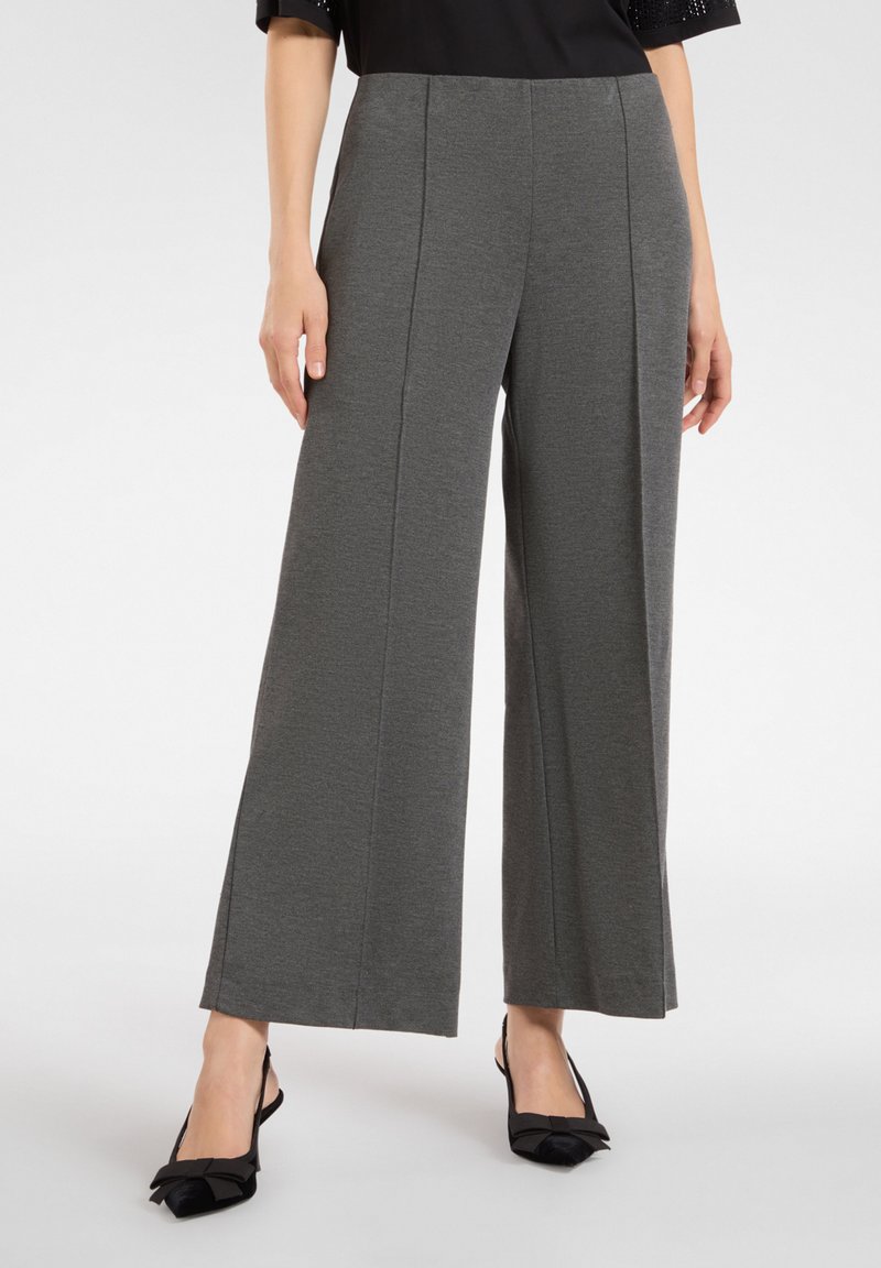 Spodnie o szerokich nogawkach w ciemnoszarym materiale, z gładką teksturą i fałdami z przodu. Zestawione z czarnymi butami z kokardką.