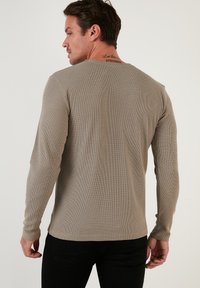 Long-sleeve, ribbed shirt in a muted taupe color, featuring a crew neck and fitted design. The fabric has a textured appearance.