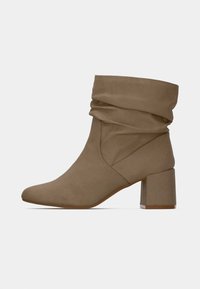 Taupe členková čižma s mäkkým zvrškom, špicatou špičkou a robustným obdĺžnikovým podpätkom. Vyrobená z mäkkej látky s hladkým povrchom.