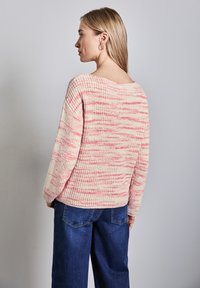 Maglione a maglia in crema con righe rosa e corallo, scollo ampio e texture a coste. Abbinato a jeans a gamba larga di colore blu scuro.