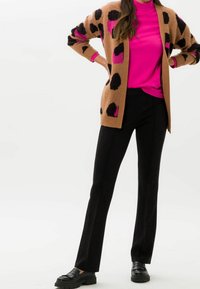 Brun cardigan med svarta och rosa leopardfläckar, bärs över en klarrosa polokrage. Svarta tighta byxor och kraftiga svarta skor.