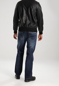 Svart läderbomberjacka med ribbade mudd, ihopparad med blå denimjeans med en urtvättad look och detaljer på bakfickorna. Svarta skor syns.